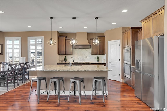 8726 Gardenia Cir, Arvada, CO 80005 - kitchen with appliances with stainless steel finishes, premium range hood, a sink, dark wood-type flooring, and a kitchen breakfast bar