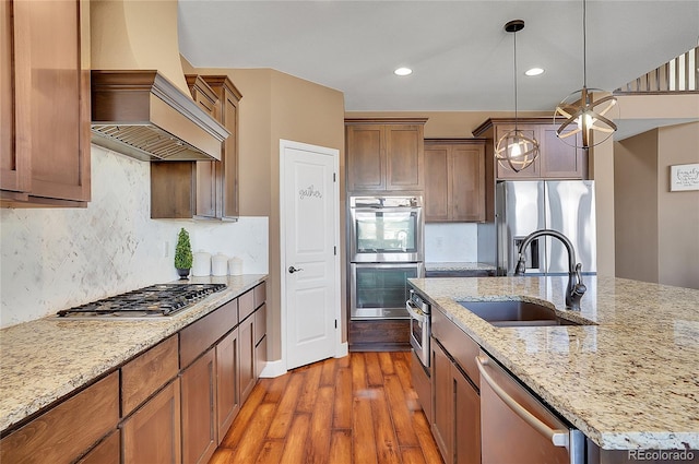 8726 Gardenia Cir, Arvada, CO 80005 - kitchen with stainless steel appliances, a sink, custom exhaust hood, wood finished floors, and decorative light fixtures