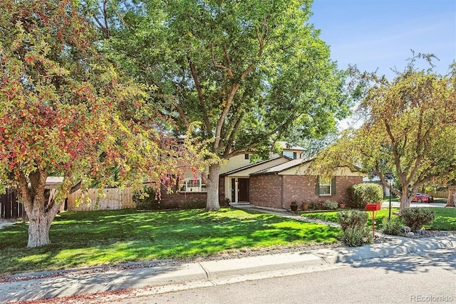 view of property exterior featuring a lawn, brick siding, and fence