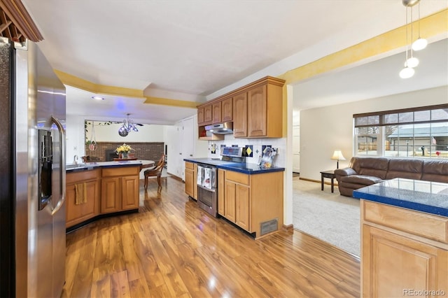 kitchen featuring under cabinet range hood, appliances with stainless steel finishes, dark countertops, open floor plan, and backsplash