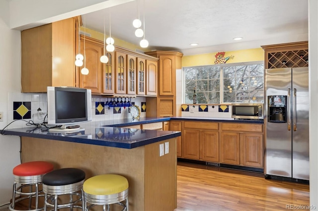 kitchen with dark countertops, glass insert cabinets, a breakfast bar area, light wood-style flooring, and stainless steel appliances