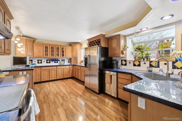 kitchen featuring light wood finished floors, glass insert cabinets, decorative backsplash, appliances with stainless steel finishes, and a sink