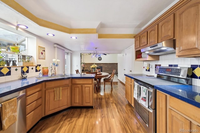 kitchen with under cabinet range hood, stainless steel appliances, light wood-style floors, and dark countertops