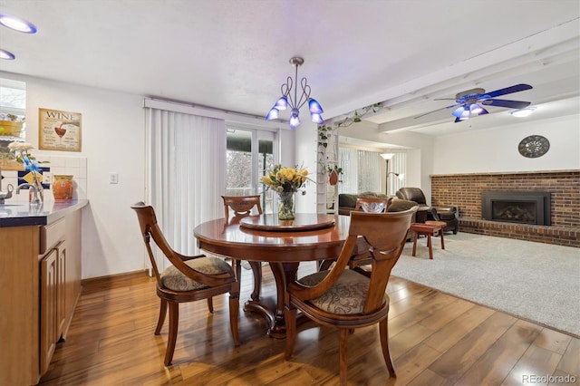 dining space with a brick fireplace, ceiling fan, and wood finished floors