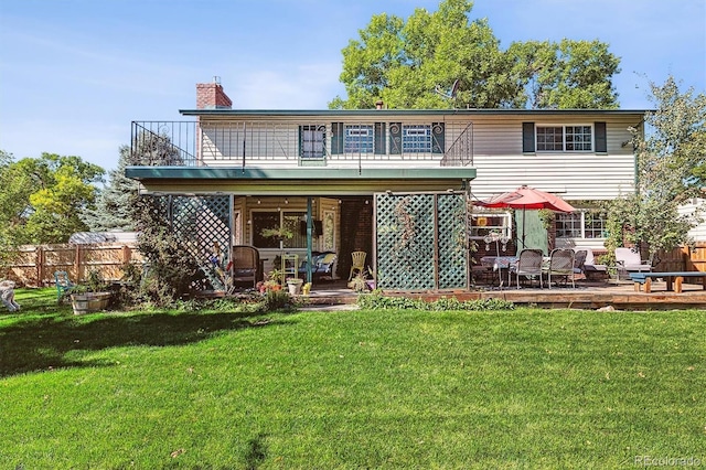 back of house featuring a patio, a balcony, fence, a chimney, and a lawn