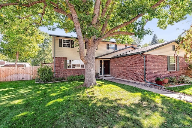 traditional-style home featuring a front yard, fence, and brick siding