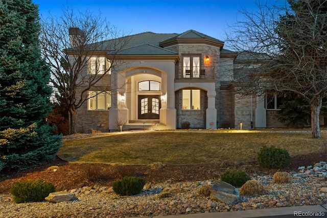 view of front of property with a balcony, stone siding, french doors, a front lawn, and stucco siding