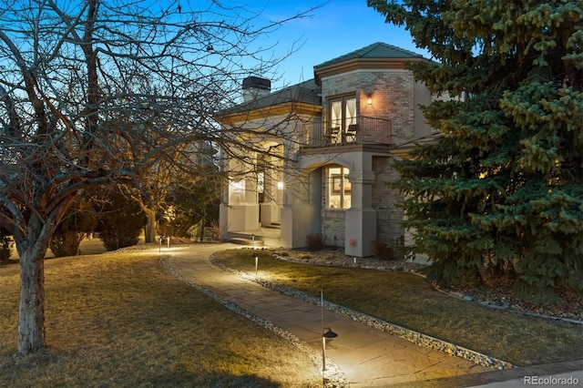 view of front of house with a balcony, a chimney, and brick siding