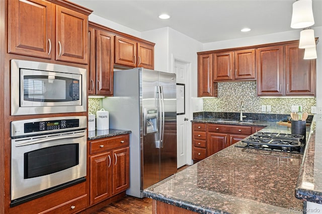 kitchen featuring appliances with stainless steel finishes, a sink, backsplash, dark wood finished floors, and brown cabinetry