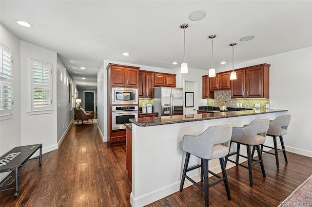 kitchen with appliances with stainless steel finishes, a peninsula, tasteful backsplash, dark stone counters, and a breakfast bar
