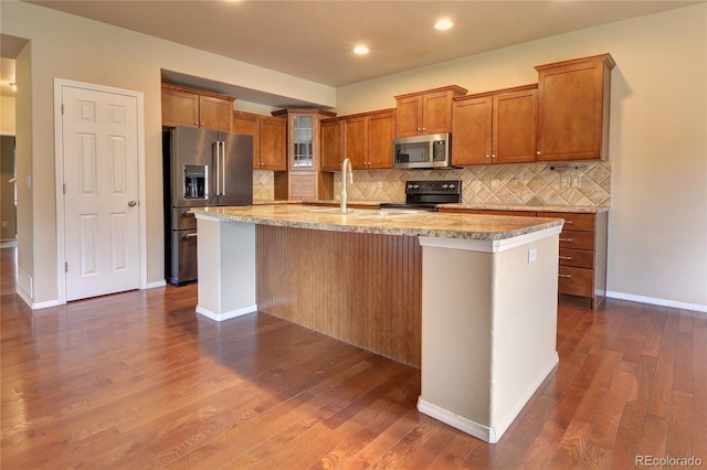 5947 Cumbre Vista Way, Colorado Springs, CO 80924 - kitchen featuring stainless steel appliances, brown cabinetry, an island with sink, backsplash, and dark wood finished floors