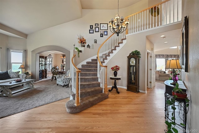 entryway with light wood finished floors, stairs, arched walkways, and an inviting chandelier