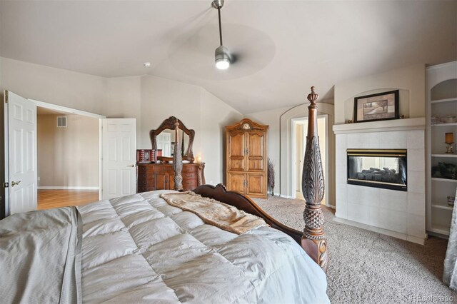 carpeted bedroom with vaulted ceiling, a tile fireplace, visible vents, and a ceiling fan