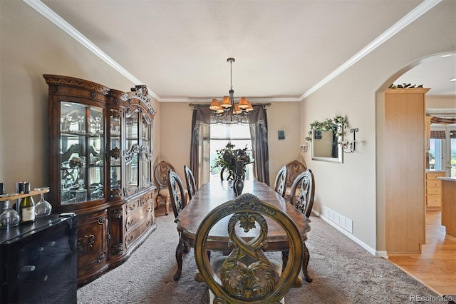 carpeted dining space featuring arched walkways, visible vents, ornamental molding, plenty of natural light, and an inviting chandelier