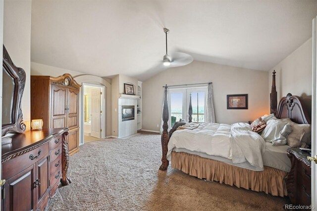 bedroom featuring baseboards, connected bathroom, a glass covered fireplace, light colored carpet, and vaulted ceiling