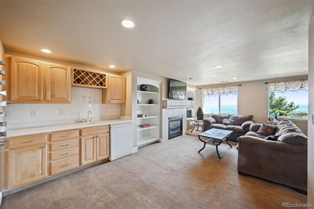 kitchen featuring light brown cabinets, light colored carpet, light countertops, dishwasher, and a tiled fireplace