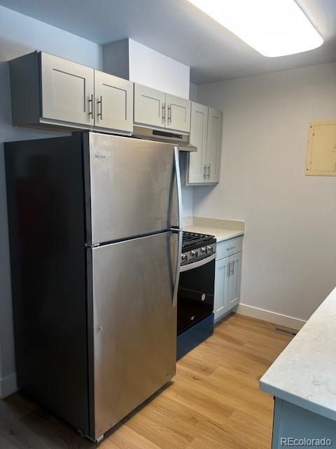 kitchen with light countertops, gray cabinets, freestanding refrigerator, light wood finished floors, and gas stove