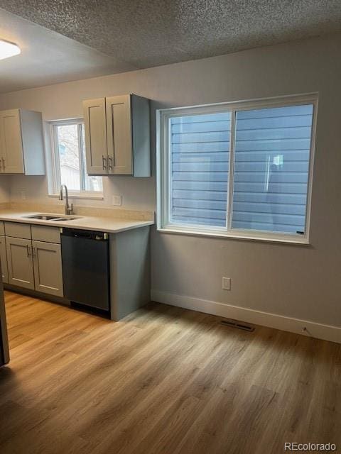 kitchen with a sink, baseboards, black dishwasher, light countertops, and light wood finished floors