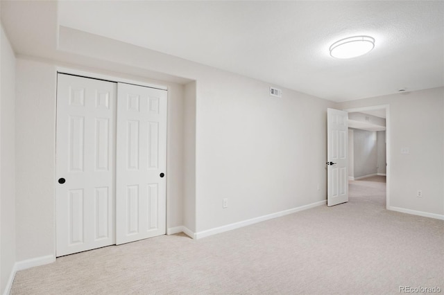 unfurnished bedroom with light colored carpet, a textured ceiling, and a closet