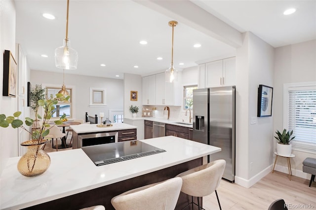 kitchen featuring light hardwood / wood-style flooring, appliances with stainless steel finishes, white cabinetry, tasteful backsplash, and decorative light fixtures