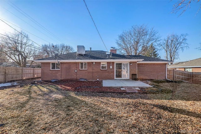 rear view of house featuring brick siding, a shingled roof, a chimney, a fenced backyard, and a patio area