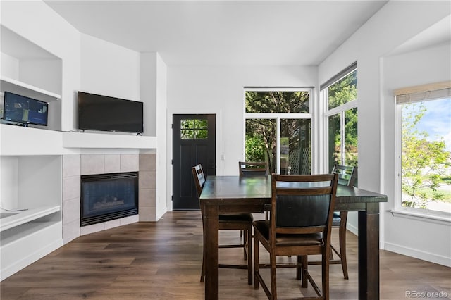 dining area with healthy amount of natural light, dark wood finished floors, a tiled fireplace, and baseboards