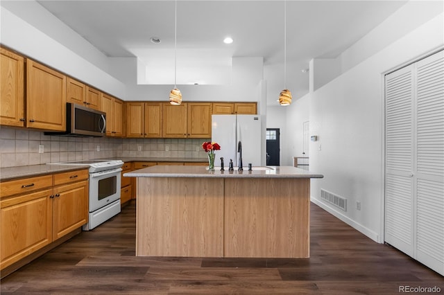 kitchen featuring white appliances, a kitchen island with sink, a sink, decorative backsplash, and recessed lighting