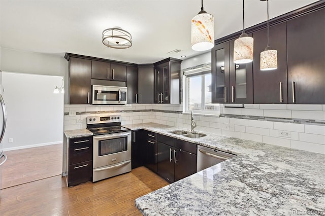 kitchen with a sink, tasteful backsplash, light wood-style floors, appliances with stainless steel finishes, and light stone countertops