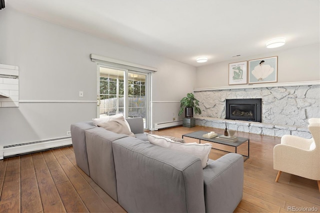 living area with a baseboard heating unit, a stone fireplace, and hardwood / wood-style floors