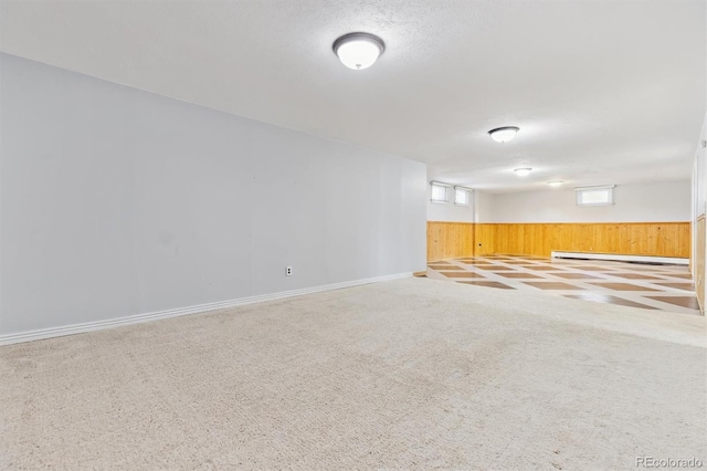 basement with a textured ceiling, carpet floors, wood walls, wainscoting, and a baseboard radiator