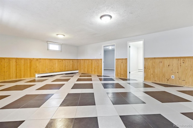 below grade area with a baseboard heating unit, wood walls, wainscoting, tile patterned floors, and a textured ceiling