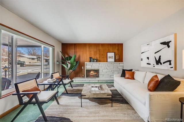 living room featuring a stone fireplace and wood walls