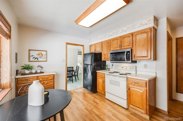 kitchen with black fridge, light wood-type flooring, and white range with electric stovetop