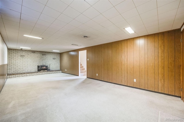 basement with a wood stove, light colored carpet, brick wall, and wood walls