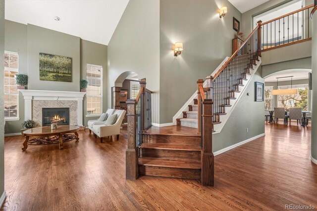 staircase featuring baseboards, arched walkways, wood finished floors, and high vaulted ceiling