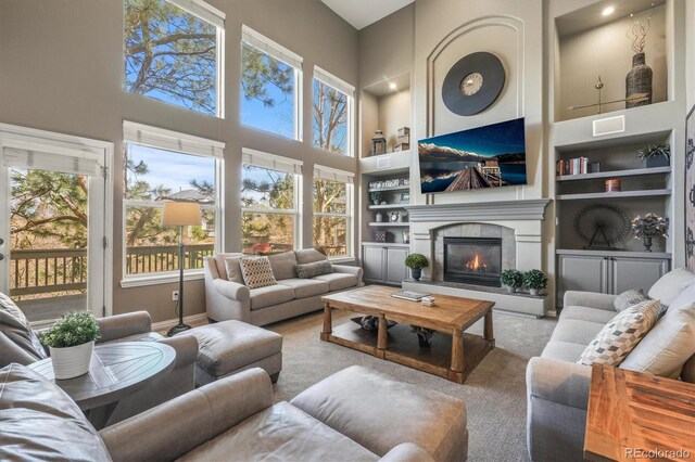 living area with a high ceiling, built in shelves, a healthy amount of sunlight, and a fireplace