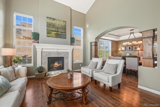 living area featuring arched walkways, a tile fireplace, high vaulted ceiling, baseboards, and dark wood-style floors