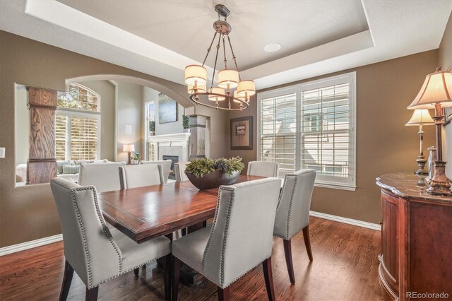dining space with arched walkways, baseboards, a healthy amount of sunlight, and a raised ceiling