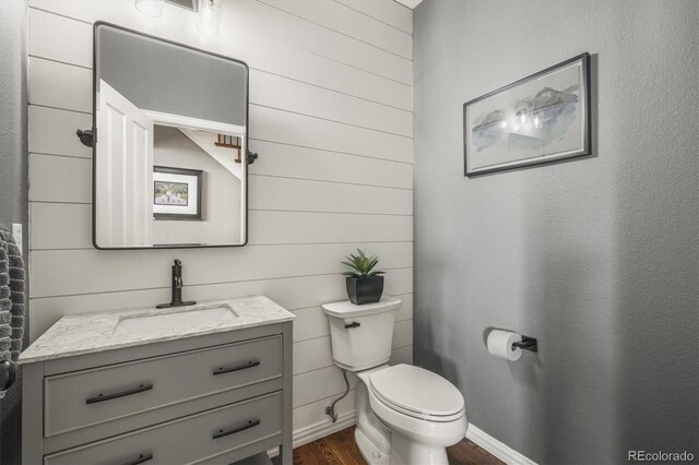 half bath with wooden walls, toilet, wood finished floors, and vanity