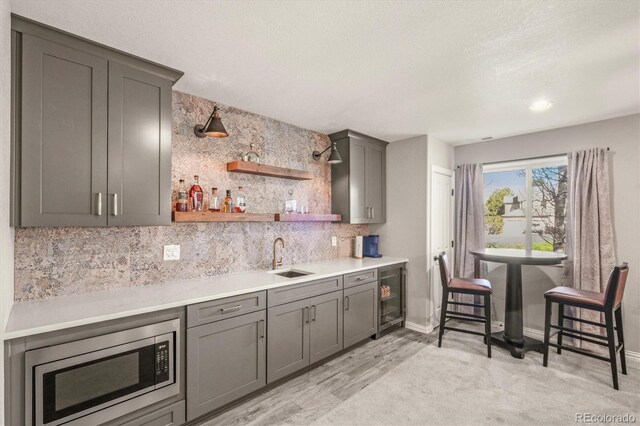bar featuring decorative backsplash, wine cooler, indoor wet bar, stainless steel microwave, and a sink