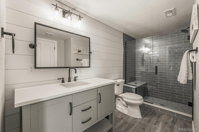 bathroom featuring vanity, wood finished floors, toilet, a textured ceiling, and a stall shower