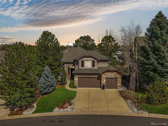 view of front of property with an attached garage, stone siding, stucco siding, a lawn, and driveway