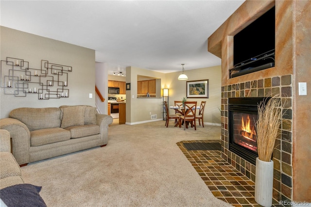 living area featuring visible vents, baseboards, light colored carpet, and a stone fireplace