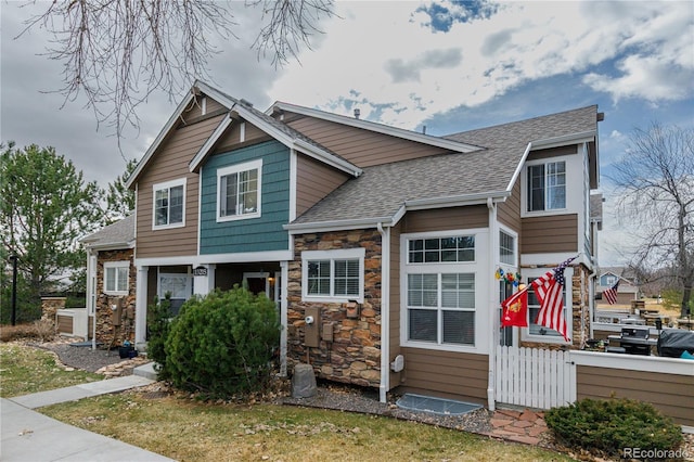 view of front of property featuring fence, stone siding, and roof with shingles