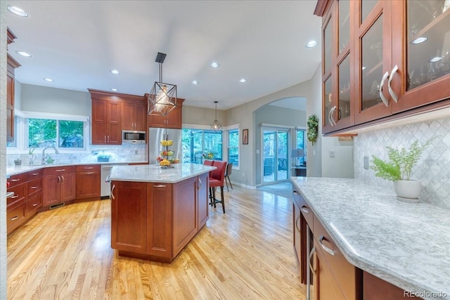 16642 W Archer Ave, Golden, CO 80401 - kitchen featuring stainless steel appliances, tasteful backsplash, light wood-type flooring, arched walkways, and a kitchen island
