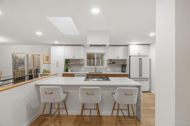 kitchen featuring a skylight, backsplash, white appliances, a kitchen bar, and white cabinets