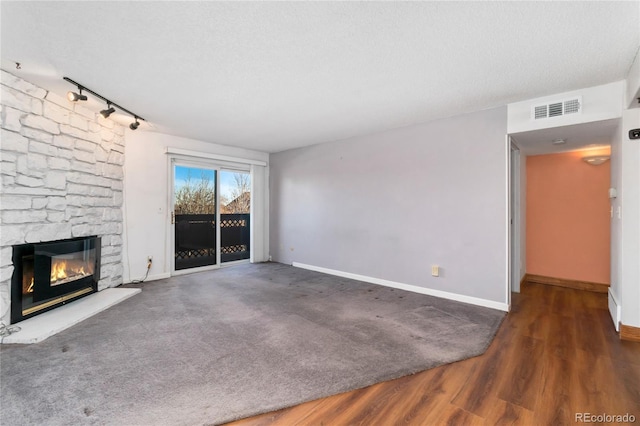 unfurnished living room with visible vents, baseboards, a stone fireplace, rail lighting, and a textured ceiling