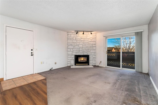 unfurnished living room with a stone fireplace, track lighting, carpet flooring, and a textured ceiling