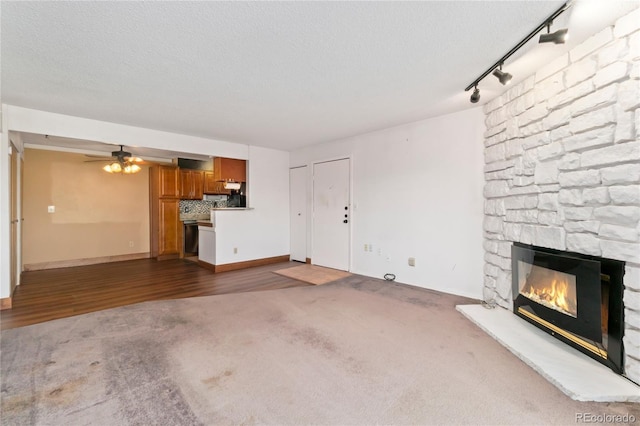 unfurnished living room featuring a stone fireplace, carpet flooring, a textured ceiling, and ceiling fan