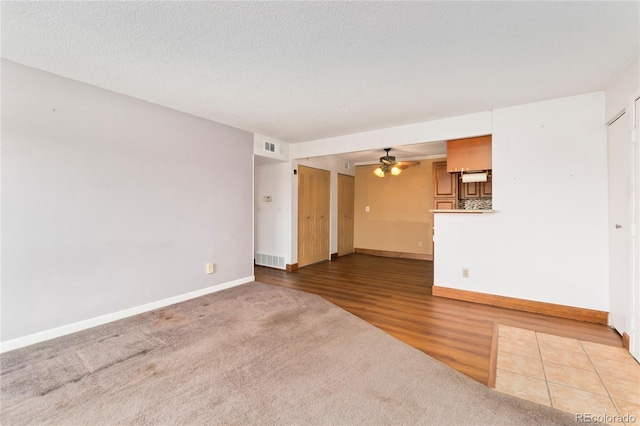 unfurnished living room featuring wood finished floors, a ceiling fan, visible vents, baseboards, and a textured ceiling